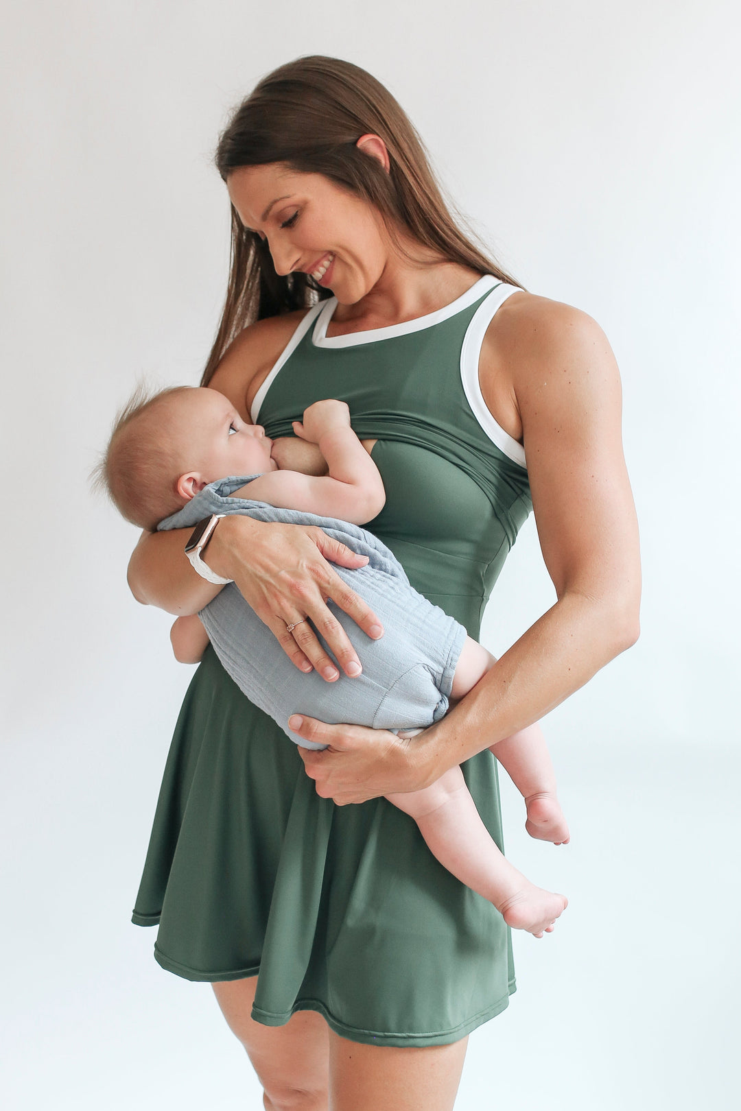 Woman in a green breastfeeding dress nursing a baby against a white background